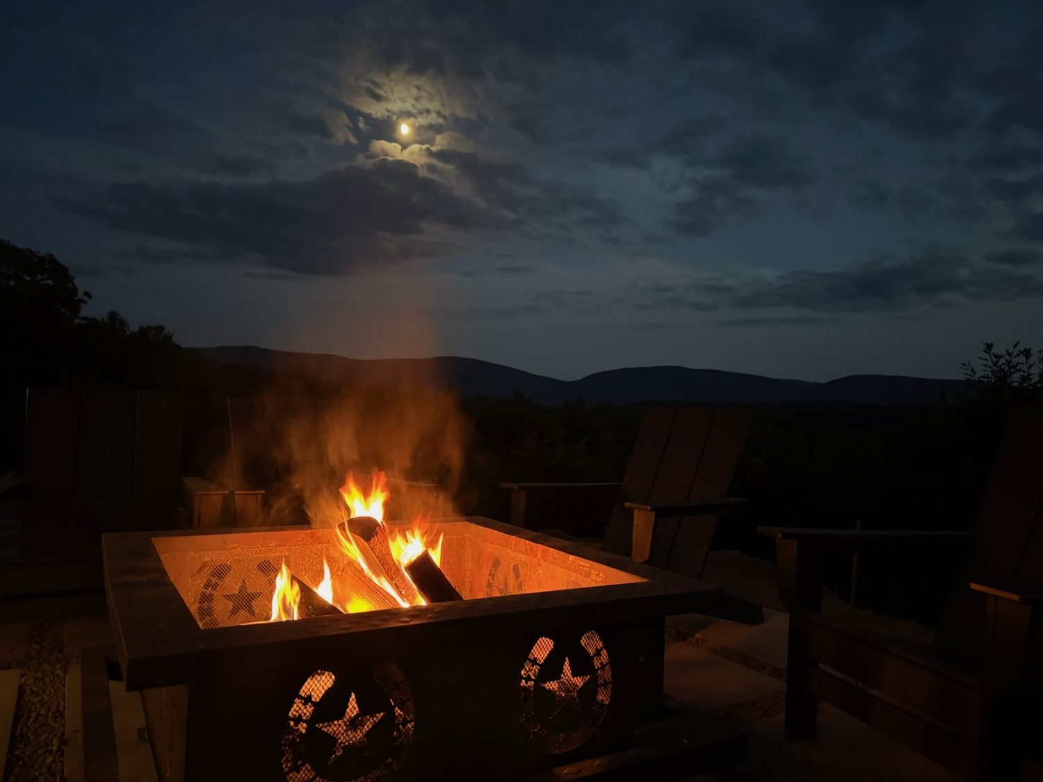 The amphitheater fire pit burning under a full moon with the Catskills behind